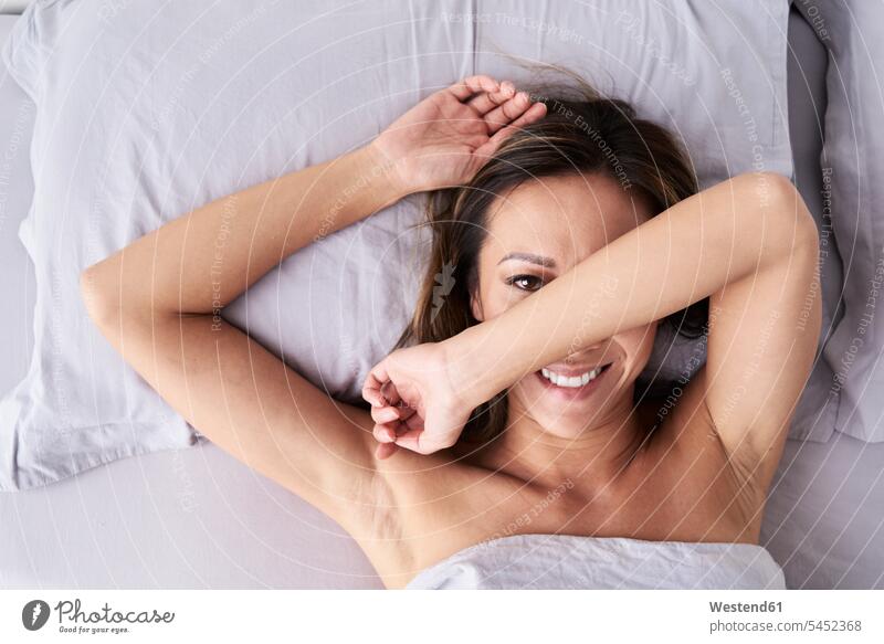 Porträt einer lächelnden Frau, die im Bett liegt und ihr Gesicht verbirgt liegen liegend weiblich Frauen Portrait Porträts Portraits Betten verstecken Gesichter
