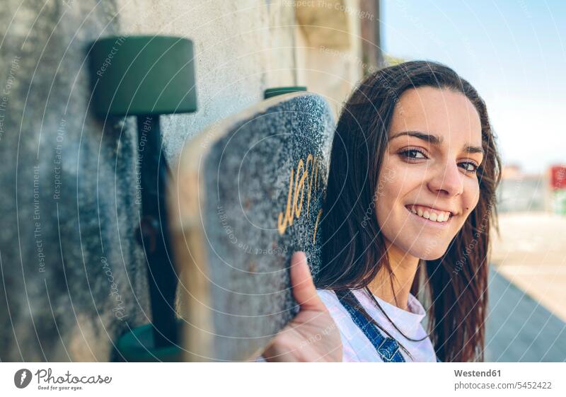 Porträt einer lächelnden jungen Frau mit Skateboard auf den Schultern Portrait Porträts Portraits Huckepack Rollbretter Skateboards weiblich Frauen