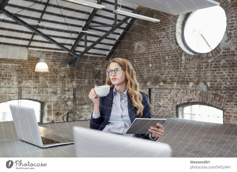 Geschäftsfrau mit Tasse Kaffee und Tablette bei Tisch in einem Loft Geschäftsfrauen Businesswomen Businessfrauen Businesswoman Tablet Computer Tablet-PC
