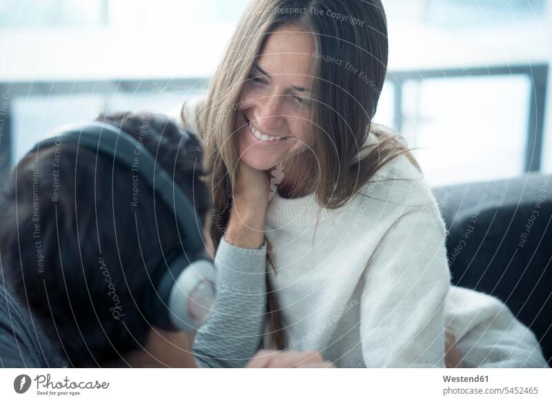 Lächelnde junge Frau schaut den Mann an, der zu Hause Kopfhörer trägt entspannt entspanntheit relaxt lächeln Kopfhoerer Paar Pärchen Paare Partnerschaft