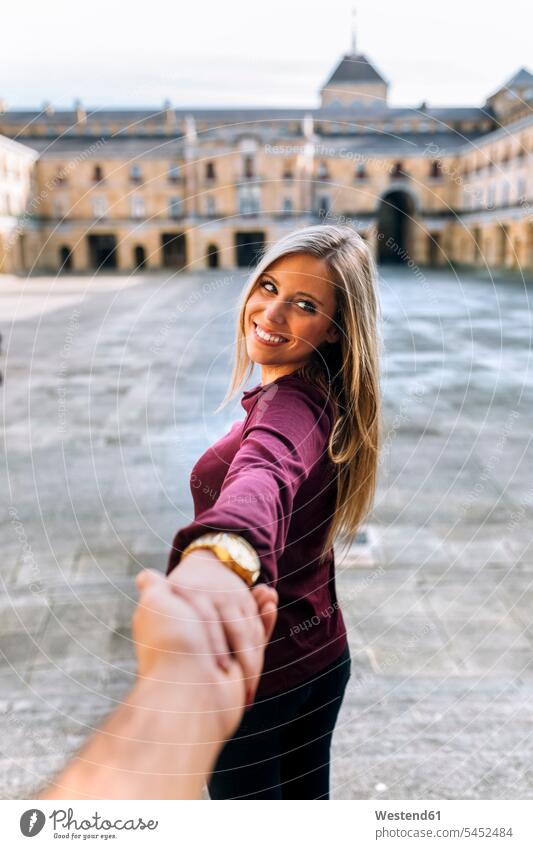 Glückliche junge Frau hält Hand auf städtischem Platz lächeln weiblich Frauen Paar Pärchen Paare Partnerschaft Erwachsener erwachsen Mensch Menschen Leute