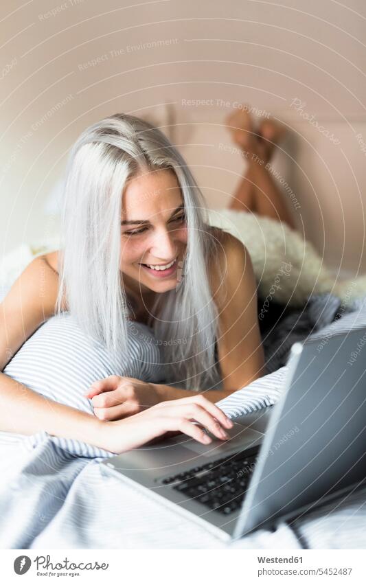 Lächelnde junge Frau liegt mit Laptop im Bett liegen liegend lächeln Betten Notebook Laptops Notebooks weiblich Frauen Computer Rechner Erwachsener erwachsen