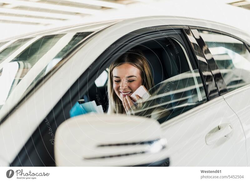 Lächelnde junge Frau mit Handy im Auto lächeln weiblich Frauen Wagen PKWs Automobil Autos Mobiltelefon Handies Handys Mobiltelefone Erwachsener erwachsen Mensch