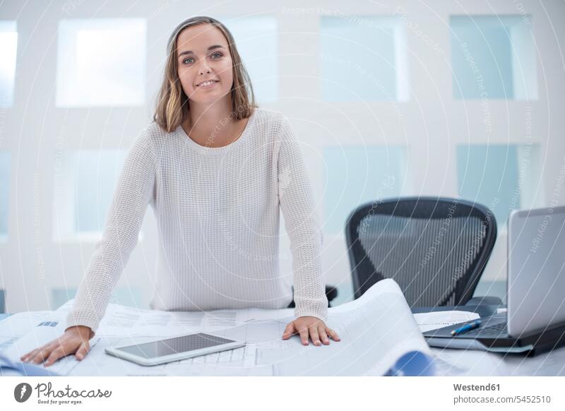 Junge Frau steht am Schreibtisch mit Laptop und digitalem Tablett Europäer Kaukasier Europäisch kaukasisch arbeiten Arbeit offenes Lächeln lachen