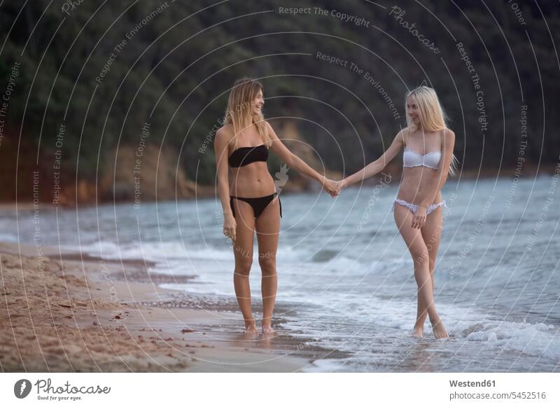 Zwei junge Frauen gehen Hand in Hand am Strand gehend geht Freundinnen glücklich Glück glücklich sein glücklichsein Meer Meere Paar Pärchen Paare Partnerschaft