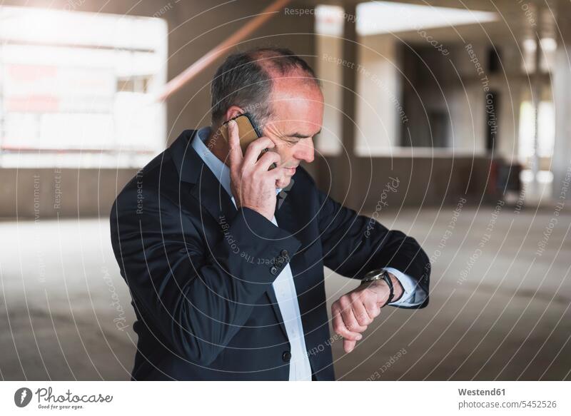 Geschäftsmann am Handy in einem im Bau befindlichen Gebäude, um die Uhrzeit zu überprüfen telefonieren anrufen Anruf telephonieren Armbanduhr Armbanduhren Mann