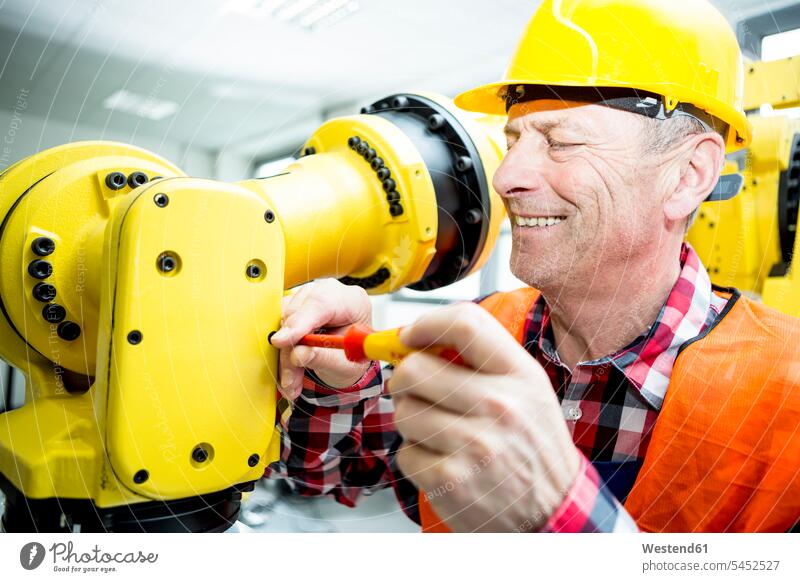 Lächelnder Techniker, der an einem Industrieroboter arbeitet Fabrik Fabriken lächeln arbeiten Arbeit industriell Gewerbe Industrien Facharbeiter Automatisierung
