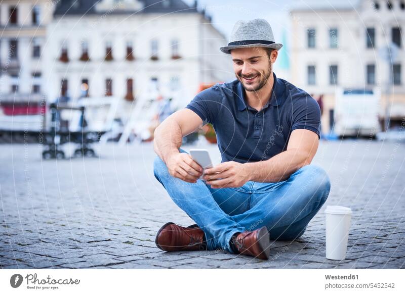 Mann sitzt auf Stadtplatz und benutzt Telefon glücklich Glück glücklich sein glücklichsein Männer männlich sitzen sitzend lächeln Handy Mobiltelefon Handies