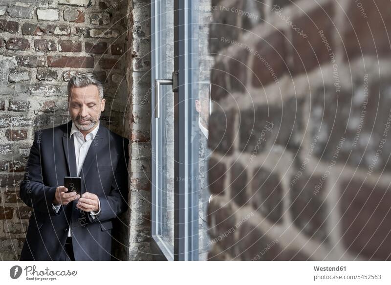 Geschäftsmann an einer Backsteinmauer beim Handy-Check Businessmann Businessmänner Geschäftsmänner Mobiltelefon Handies Handys Mobiltelefone lächeln