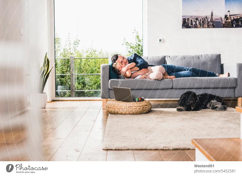 Vater kuschelt mit seiner Tochter auf der Couch Hund Hunde umarmen Umarmung Umarmungen Arm umlegen Töchter Zuhause zu Hause daheim Laptop Notebook Laptops