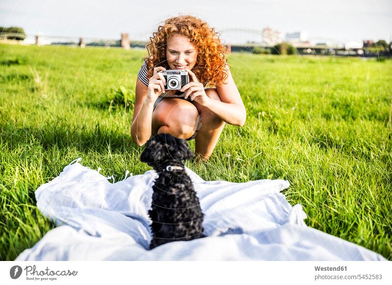 Deutschland, Köln, Porträt einer lächelnden jungen Frau auf einer Wiese, die ihren Hund fotografiert weiblich Frauen fotografieren Hunde Erwachsener erwachsen