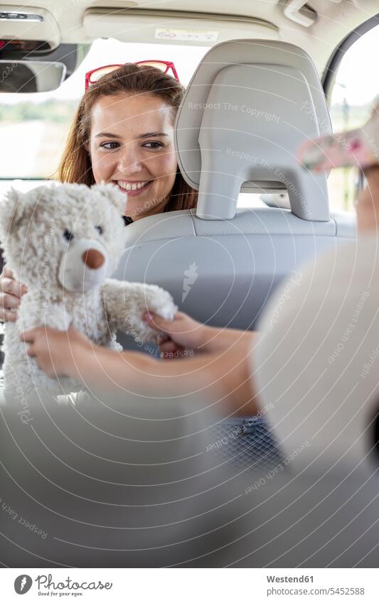 Mutter schaut Tochter beim Spielen mit Teddybär an, die eine Autoreise macht lächeln Mädchen weiblich spielen sitzen sitzend sitzt halten Wagen PKWs Automobil