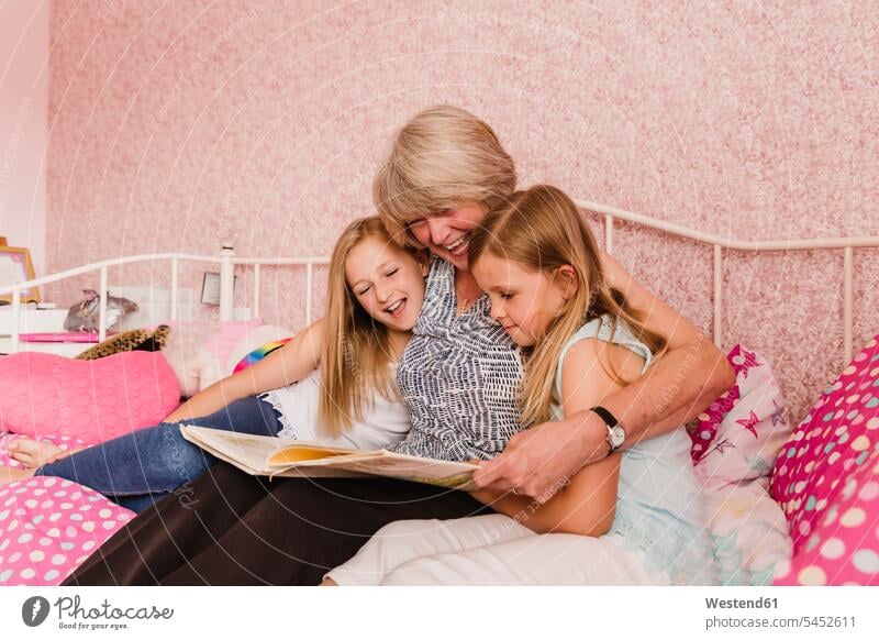 Großmutter sitzt mit ihren Enkeltöchtern im Bett und liest ein Buch Enkelin Enkeltochter Enkelinnen Grossmutter Oma Grossmama Großmütter Omi Bücher Enkelkind