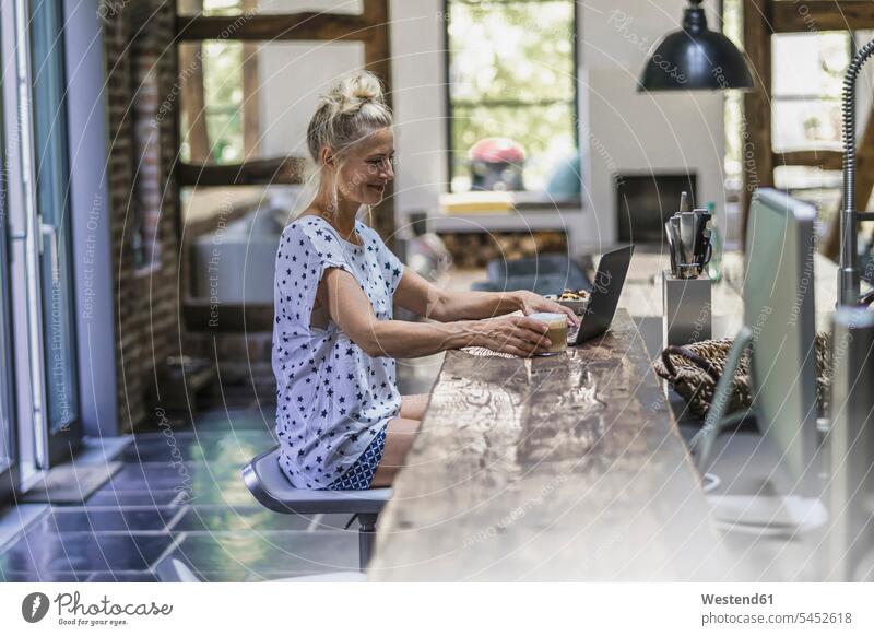 Frau sitzt in der Küche und benutzt Laptop sitzen sitzend Kaffee arbeiten Arbeit trinken morgens Morgen früh Frühe Notebook Laptops Notebooks weiblich Frauen