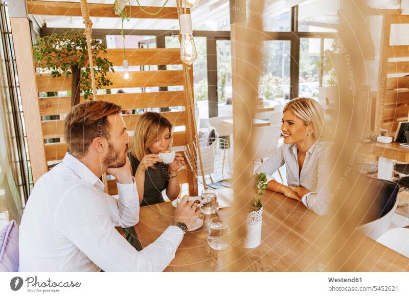 Drei Freunde treffen sich in einem Cafe sprechen reden Kaffeehaus Bistro Cafes Café Cafés Kaffeehäuser lächeln Freundschaft Kameradschaft Gastronomie hölzern