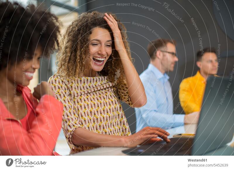 Zwei glückliche Frauen im Büro teilen sich einen Laptop Office Büros Notebook Laptops Notebooks lächeln lachen Kollegin Kolleginnen Arbeitsplatz Arbeitsstätte