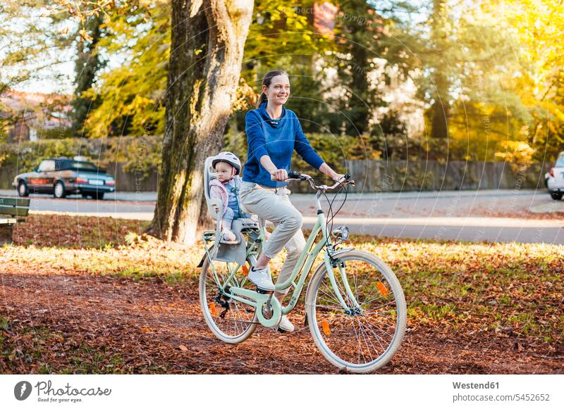 Mutter und Tochter fahren Fahrrad, das Baby trägt einen Helm und sitzt im Kindersitz Bikes Fahrräder Räder Rad lachen radfahren fahrradfahren radeln Fahrradhelm