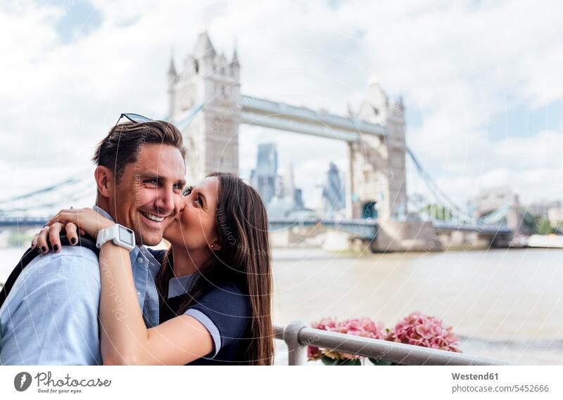 UK, London, glückliches Paar küsst sich mit der Tower Bridge im Hintergrund küssen Küsse Kuss lächeln umarmen Umarmung Umarmungen Arm umlegen Pärchen Paare