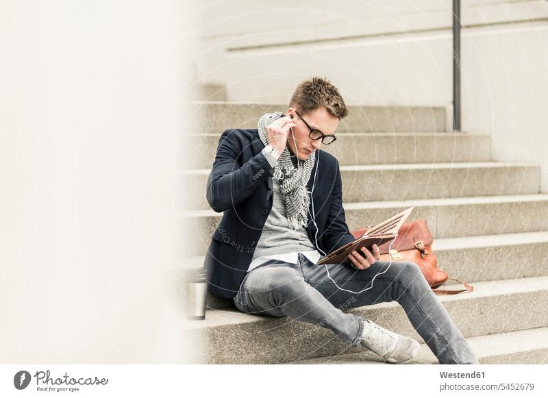 Junger Geschäftsmann sitzt auf einer Treppe und benutzt ein digitales Tablett Urban städtisch Urbanität Urbanitaet unterwegs auf Achse in Bewegung jung