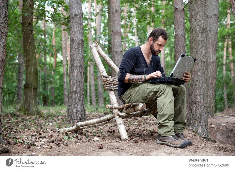 Mann sitzt mit Laptop auf selbstgebautem Holzstuhl im Wald Notebook Laptops Notebooks Männer männlich Forst Wälder sitzen sitzend Computer Rechner Erwachsener
