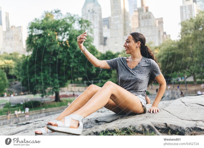 USA, Manhattan, lächelnde junge Frau macht Selfie mit Smartphone im Central Park iPhone Smartphones weiblich Frauen Selfies Handy Mobiltelefon Handies Handys