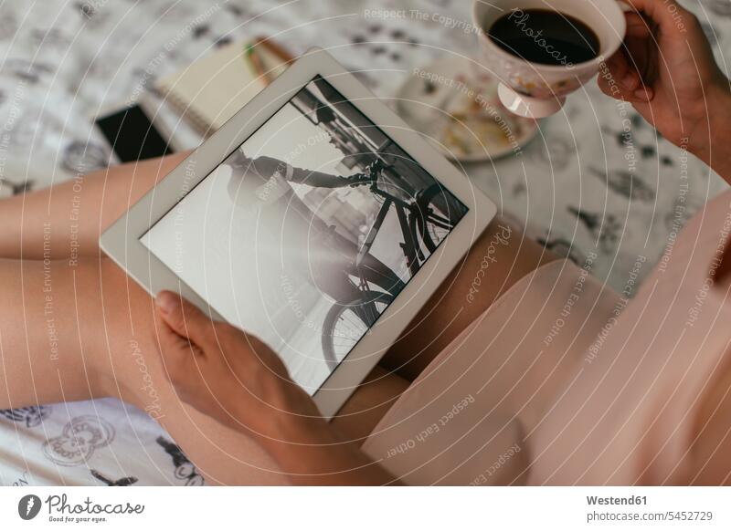 Frau sitzt im Bett und schaut sich Fotos auf dem Tablett an weiblich Frauen Kaffeetasse Kaffeetassen Betten sitzen sitzend Tablet Computer Tablet-PC Tablet PC