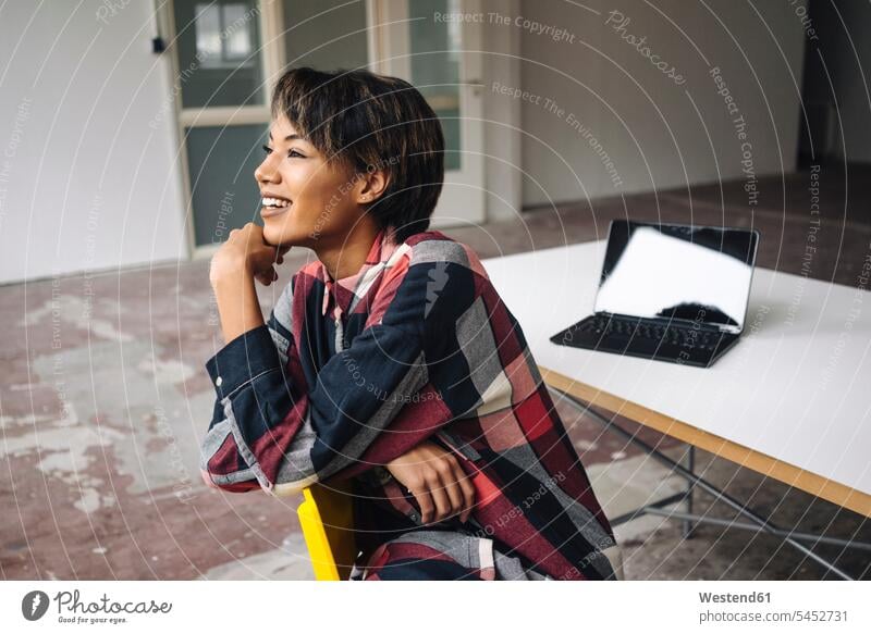 Lächelnde Frau auf Stuhl sitzend mit Laptop auf Tisch Geschäftsfrau Geschäftsfrauen Businesswomen Businessfrauen Businesswoman lächeln Notebook Laptops