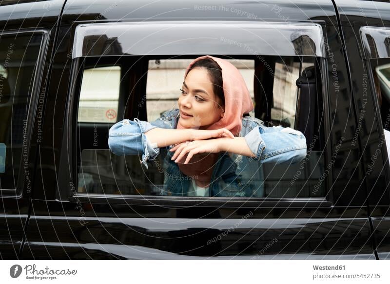Großbritannien, England, London, junge Frau mit Hijab, die aus einem Taxi schaut lächeln weiblich Frauen Taxis Taxen Kopftuch Kopftücher muslimisch Moslem