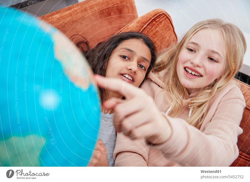 Zwei Mädchen liegen auf einer Couch und zeigen auf einen Globus Freundinnen Weltkugel Erdkugel Globen Sofa Couches Liege Sofas mit dem Finger zeigen deuten