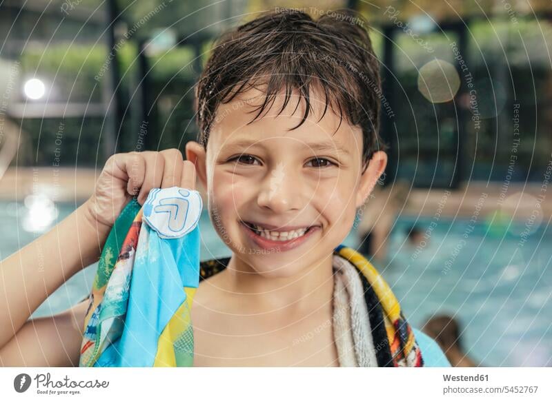 Porträt eines stolzen Jungen, der sein Schwimmabzeichen am Beckenrand eines Hallenbades zeigt Schwimmbad Schwimmbaeder Schwimmbäder Stolz stolz sein lächeln