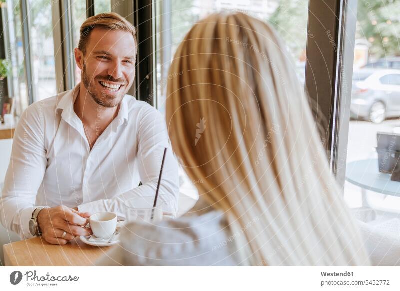 Glücklicher Mann schaut Frau in einem Café an Paar Pärchen Paare Partnerschaft Cafe Kaffeehaus Bistro Cafes Cafés Kaffeehäuser sprechen reden lachen Mensch