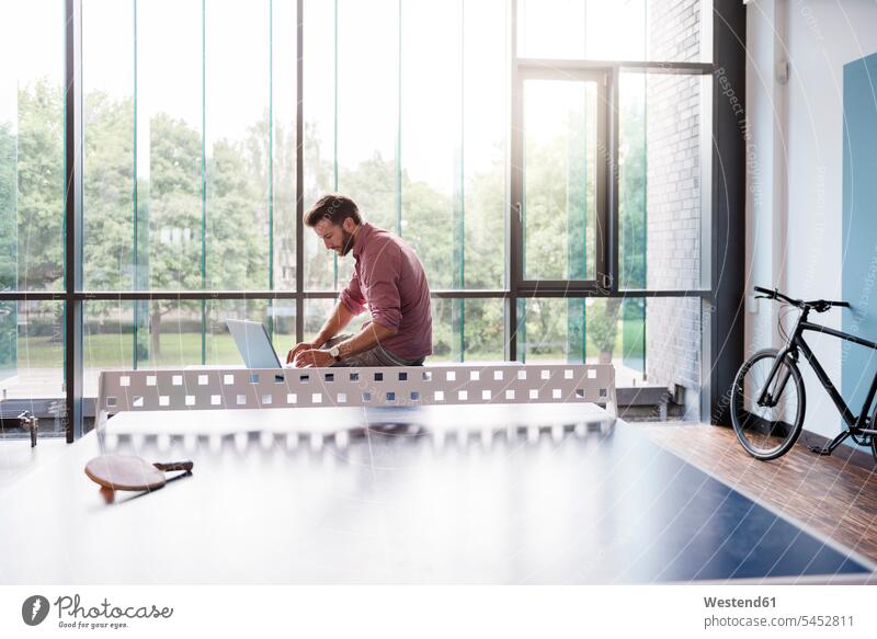 Mann mit Laptop im Pausenraum eines modernen Büros am Tischtennistisch Notebook Laptops Notebooks Männer männlich Computer Rechner Erwachsener erwachsen Mensch