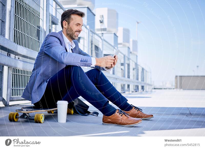 Geschäftsmann sitzt auf einem Longboard und telefoniert Handy Mobiltelefon Handies Handys Mobiltelefone sitzen sitzend Skateboard Rollbretter Skateboards