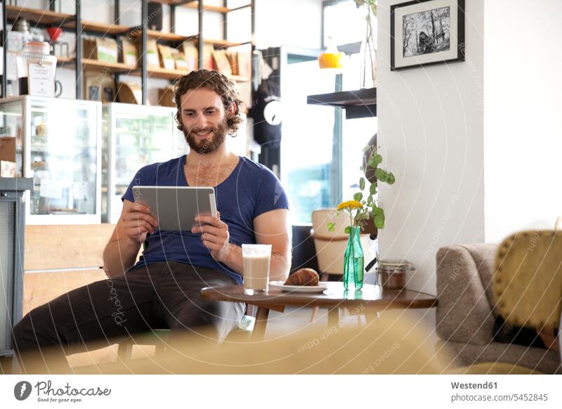 Porträt eines jungen Mannes, der mit einem Tablett in einem Café sitzt Cafe Kaffeehaus Bistro Cafes Kaffeehäuser Tablet Computer Tablet-PC Tablet PC iPad