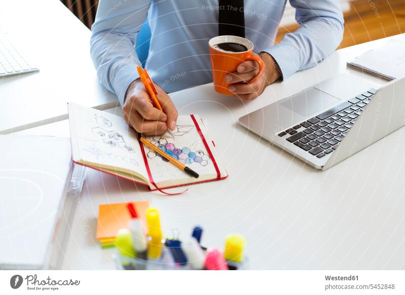 Mann zieht am Schreibtisch im Büro in ein Notizbuch zeichnen Zeichnung Arbeitstisch Schreibtische Notizbücher Notizbuecher Office Büros Tisch Tische