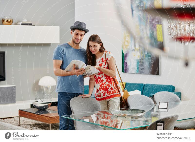 Ehepaar im Möbelgeschäft betrachtet Esstisch, schaut Katalog an Paar Pärchen Paare Partnerschaft einkaufen Einkaufen shoppen shopping Esstische aussuchen