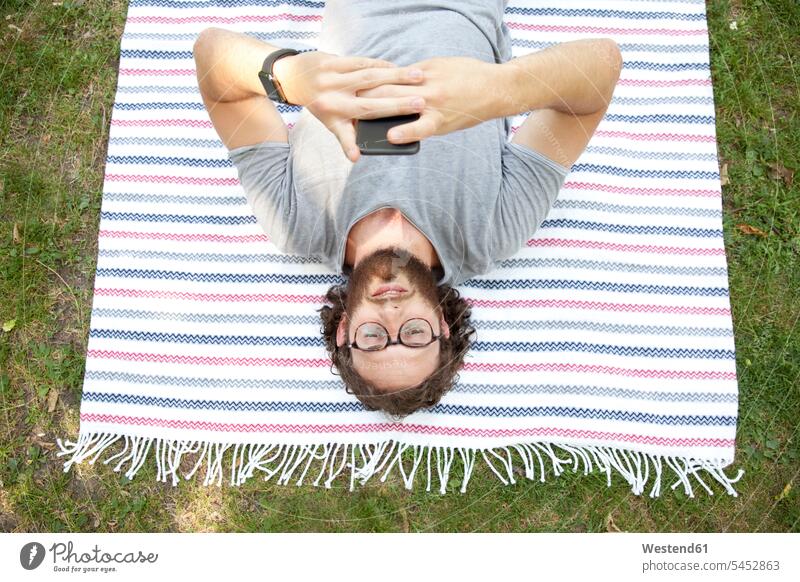 Mann liegt auf einer Decke in einem Park und benutzt ein Mobiltelefon, Draufsicht Smartphone iPhone Smartphones Männer männlich Handy Handies Handys