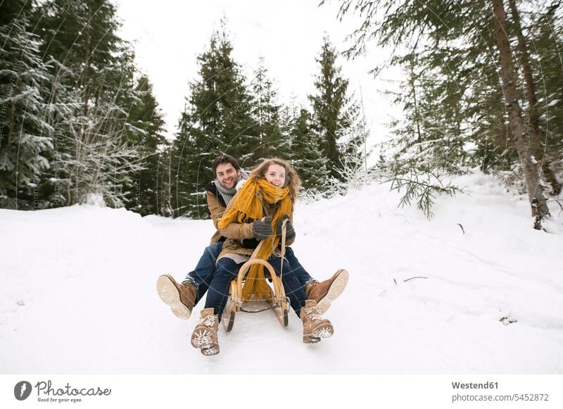 Glückliches junges Paar auf Schlitten im Winterwald schlittenfahren rodeln Schlitten fahren Pärchen Paare Partnerschaft Mensch Menschen Leute People Personen