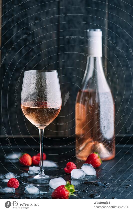 Glas gekühlten Rosenwein, Flasche, Eiswürfel und Erdbeeren und Himbeeren auf dunklem Grund eisgekühlt eisgekuehlt eisgekühlte nass Naesse Nässe