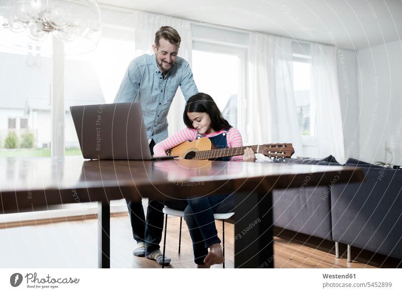Vater lächelt die Gitarre spielende Tochter vor dem Laptop an Notebook Laptops Notebooks Gitarren Töchter lächeln Papas Väter Vati Vatis Papis Computer Rechner