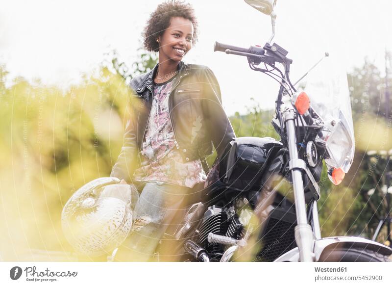 Lächelnde junge Frau mit ihrem Motorrad weiblich Frauen lächeln Motorräder Erwachsener erwachsen Mensch Menschen Leute People Personen Kraftfahrzeug