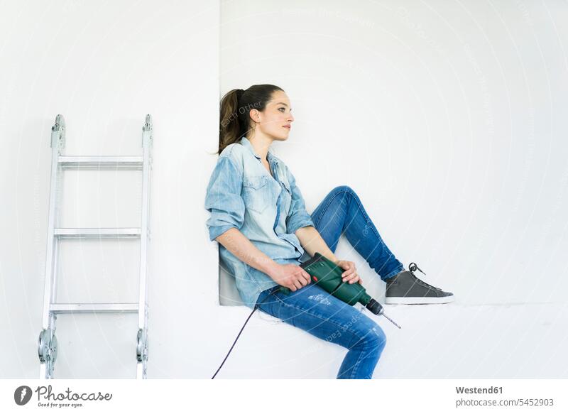 Frau sitzt in einer Nische an der Leiter mit elektrischer Bohrmaschine weiblich Frauen Umzug umziehen Schlagbohrer Bohrer Bohrmaschinen Leitern Erwachsener
