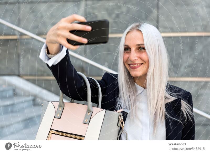 Lächelnde junge Frau, die ein Selfie auf einer Treppe in der Stadt schießt Selfies weiblich Frauen Handy Mobiltelefon Handies Handys Mobiltelefone Erwachsener