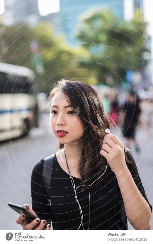 Porträt einer jungen Frau mit Kopfhörer und Handy, die etwas beobachtet weiblich Frauen Portrait Porträts Portraits Erwachsener erwachsen Mensch Menschen Leute
