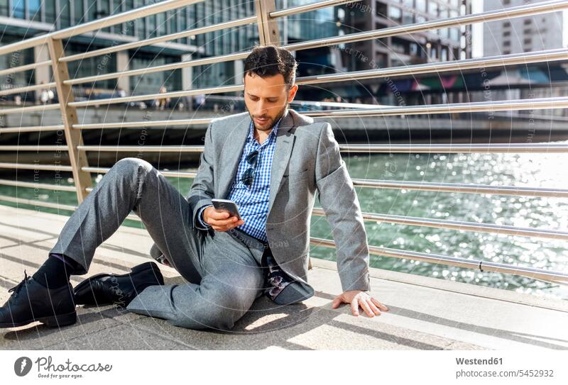 Geschäftsmann sitzt mit Handy auf einer Brücke in der Stadt Mobiltelefon Handies Handys Mobiltelefone sitzen sitzend Businessmann Businessmänner Geschäftsmänner