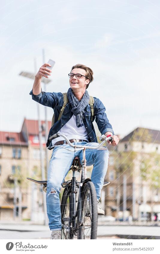 Junger Mann mit Fahrrad in der Stadt mit Handy Bikes Fahrräder Räder Rad Mobiltelefon Handies Handys Mobiltelefone glücklich Glück glücklich sein glücklichsein