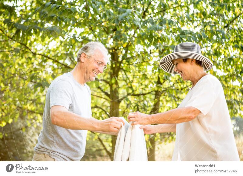 Glückliches älteres Ehepaar faltet Decke im Park Decken Paar Pärchen Paare Partnerschaft lächeln Mensch Menschen Leute People Personen Natur zusammenlegen