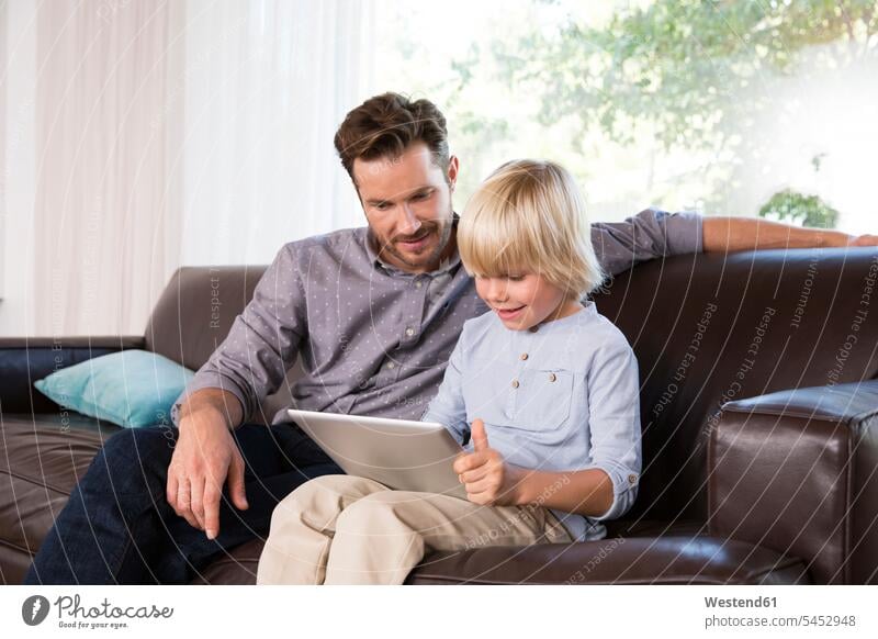 Vater und Sohn sitzen zu Hause auf der Couch und benutzen Tabletten Tablet Computer Tablet-PC Tablet PC iPad Tablet-Computer Söhne sitzend sitzt Zuhause daheim