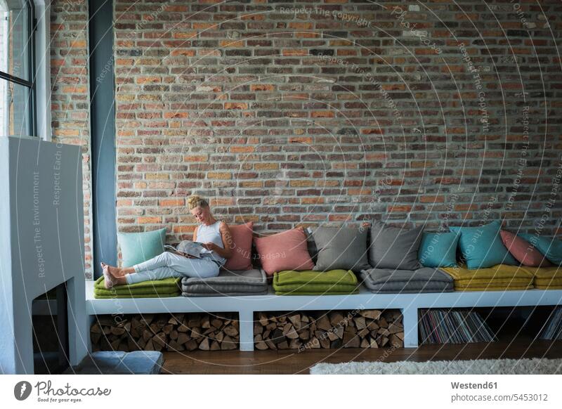 Reife Frau sitzt auf dem Sofa und liest eine Zeitschrift Zuhause zu Hause daheim lesen Lektüre Landhaus Landhäuser Landhaeuser Couches Liege Sofas Magazin