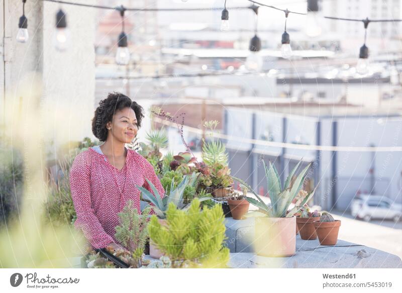 Lächelnde Frau steht in ihrem Dachgarten weiblich Frauen stehen stehend gärtnern Gartenarbeit Gartenbau Dachterrasse Dachterrassen Erwachsener erwachsen Mensch